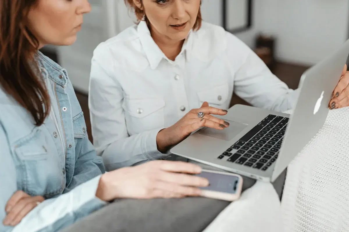 Two women having a conversation while one of them uses a laptop to display information.