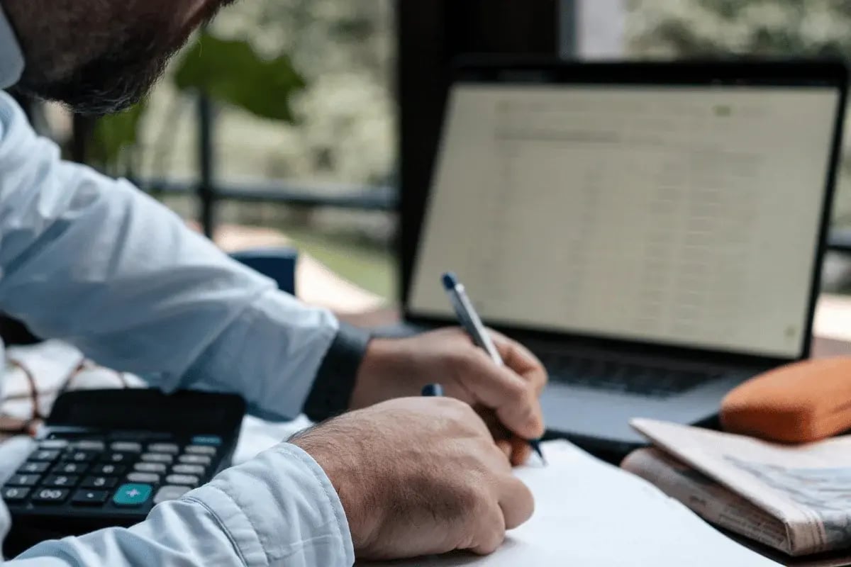 Businessman writing notes with laptop and calculator.