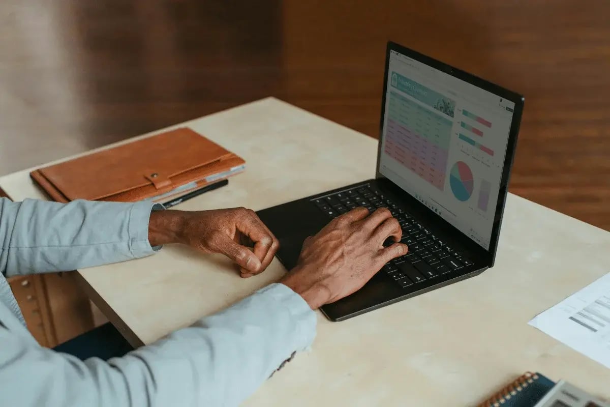Close-up of hands typing on a laptop, reviewing colorful bar and pie charts with data.