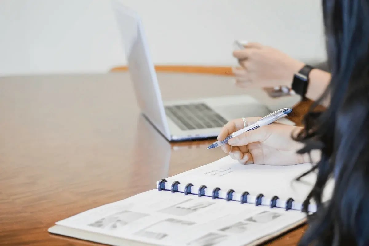 Close-up of person writing notes in a spiral notebook during meeting.
