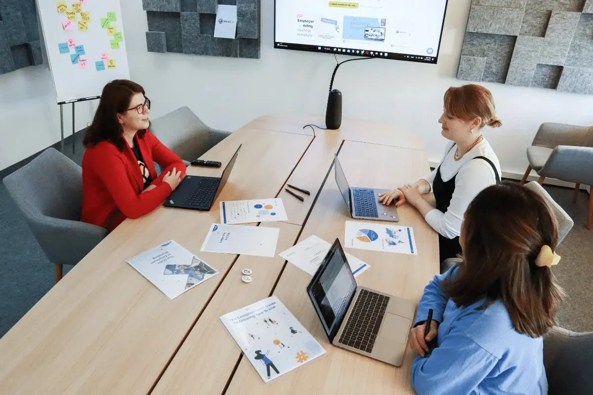 Three colleagues working together at a conference table with laptops and documents.