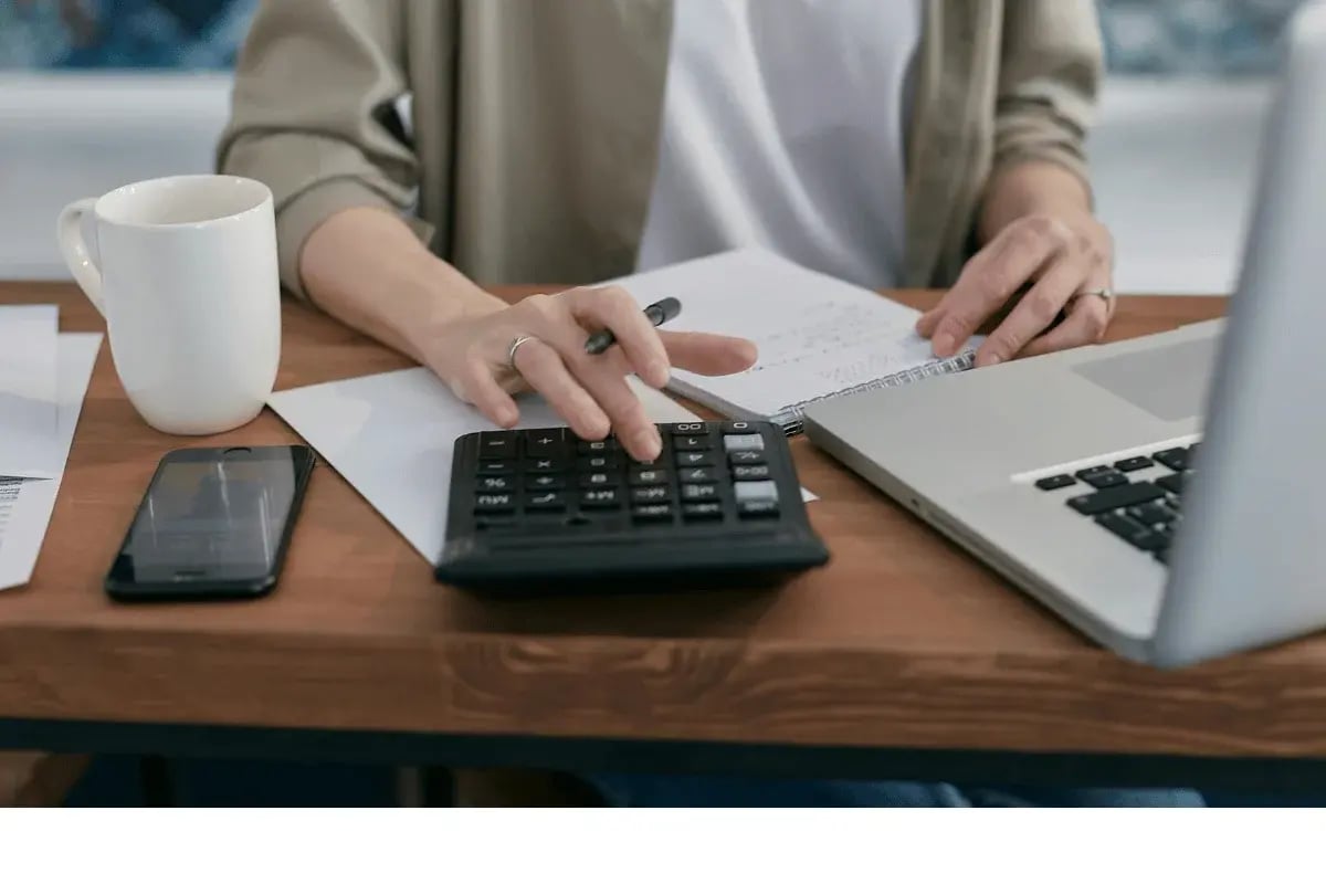 Person using a calculator beside a laptop and notebook.