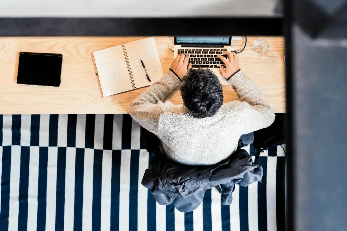 A person working on a laptop surrounded by a notebook, pen, and tablet.