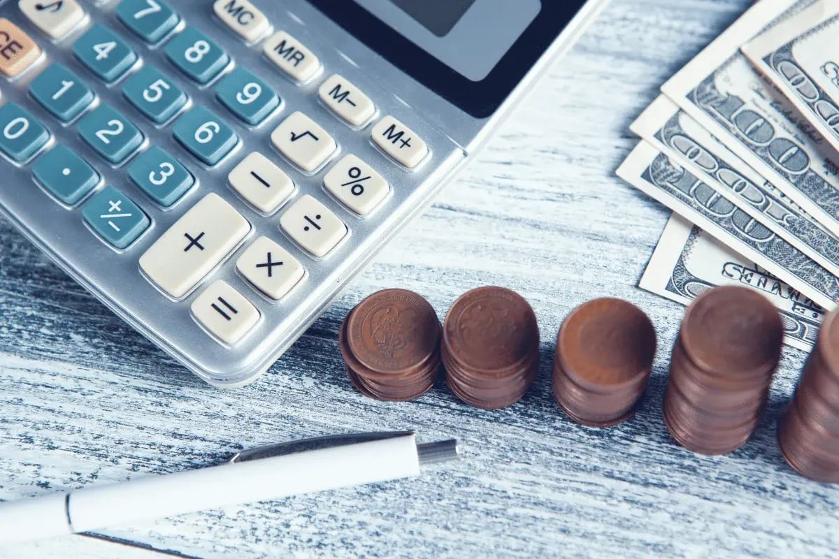 Calculator, coins, and dollar bills arranged neatly on wooden desk.