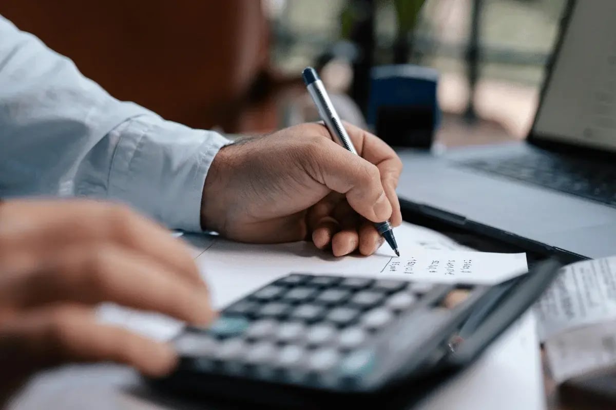 Person using a calculator and writing figures on paper.