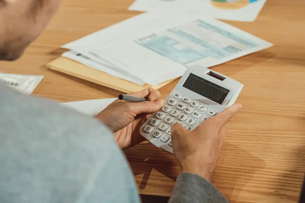 Person using a large calculator at a wooden desk with documents.