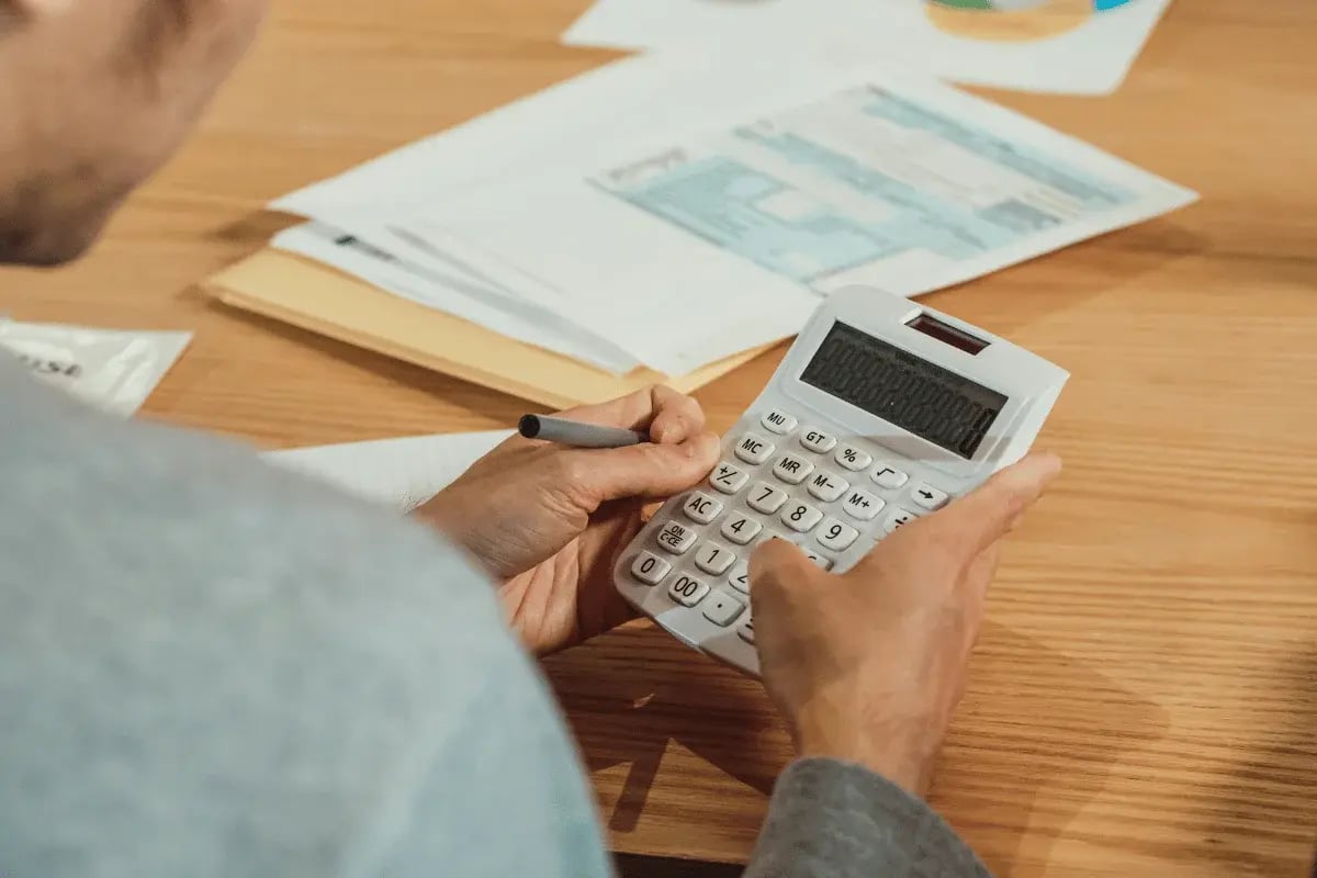 Person calculating numbers with a white calculator on desk.