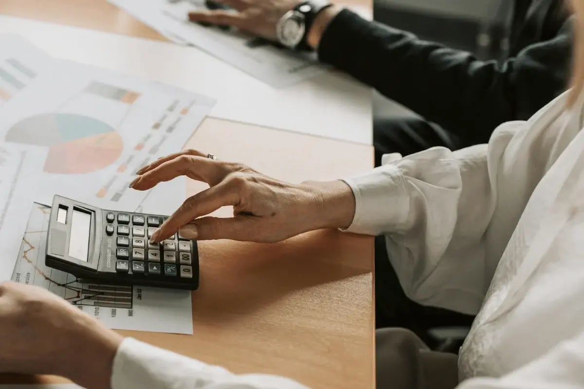 Hand pressing buttons on calculator with financial documents in the background.