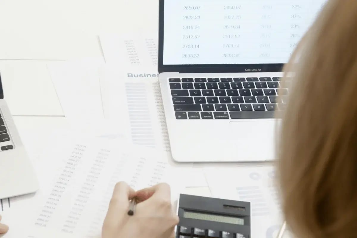Accountant reviewing numeric reports and using a calculator near a MacBook Air.