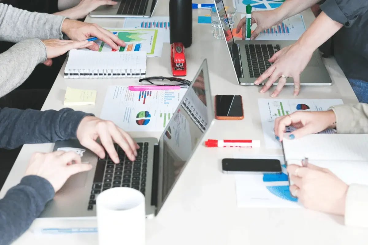 Professionals collaborate at a table, using laptops, notebooks, and colorful charts for a brainstorming session.