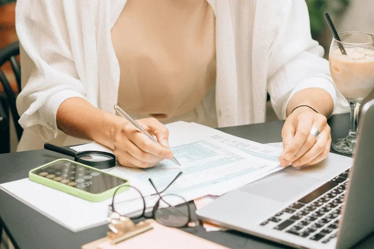 Woman working on tax documents with pen and laptop.