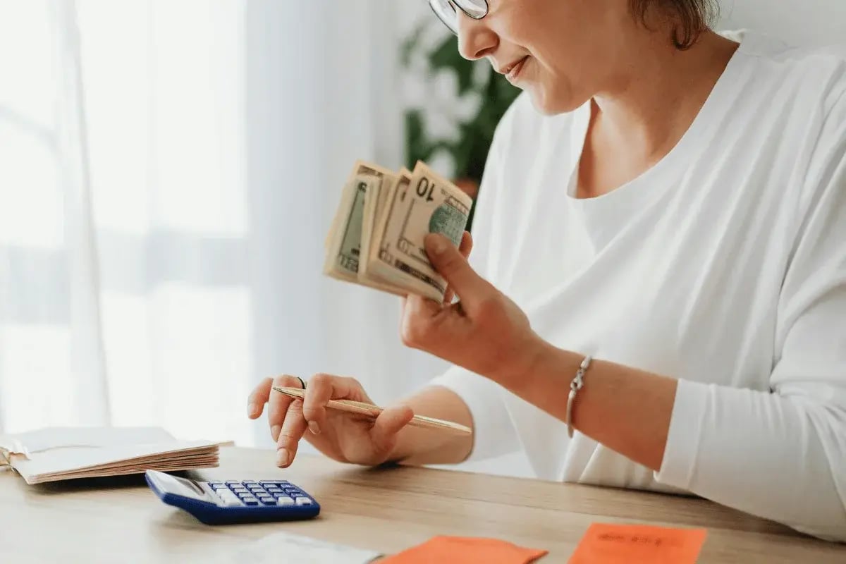 A close-up of a person calculating expenses with cash and a calculator in front of them.