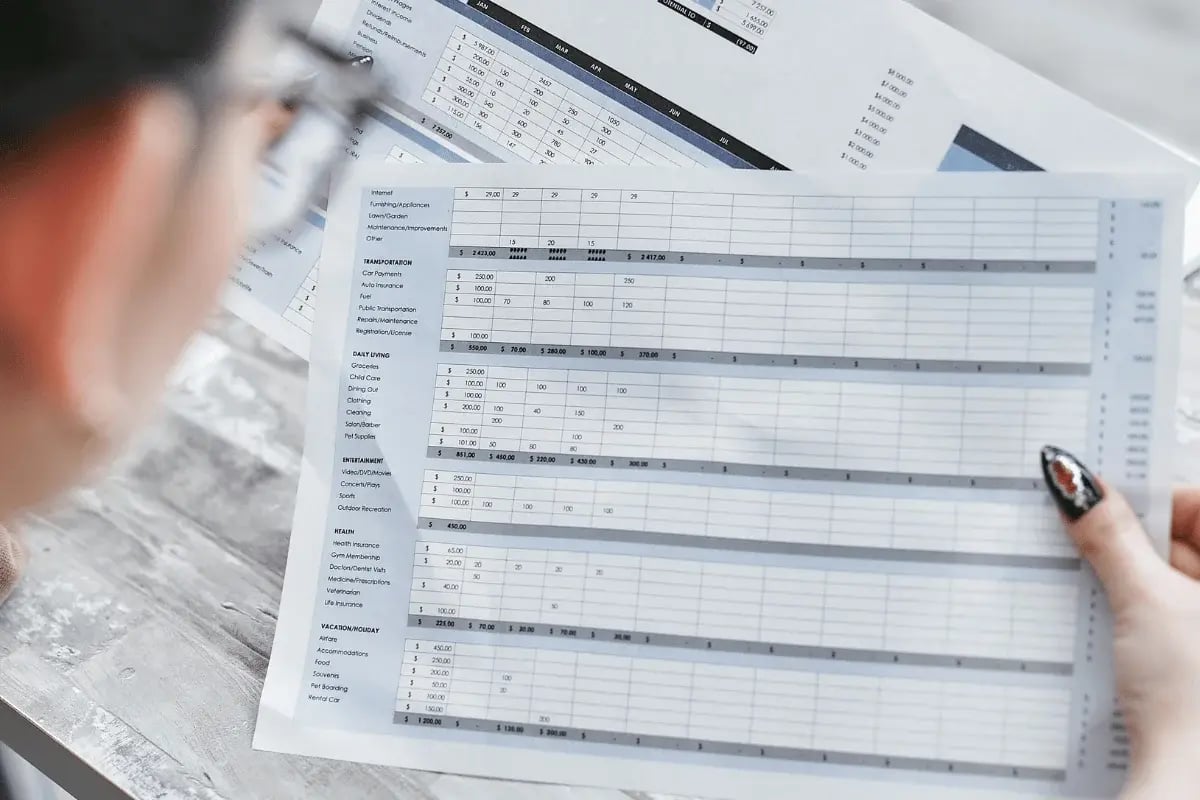 A person holds a detailed budget sheet, displaying categories for expenses like transportation, daily living, and entertainment.