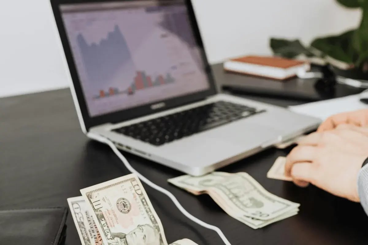 Hands handling cash in front of a financial graph on a laptop.