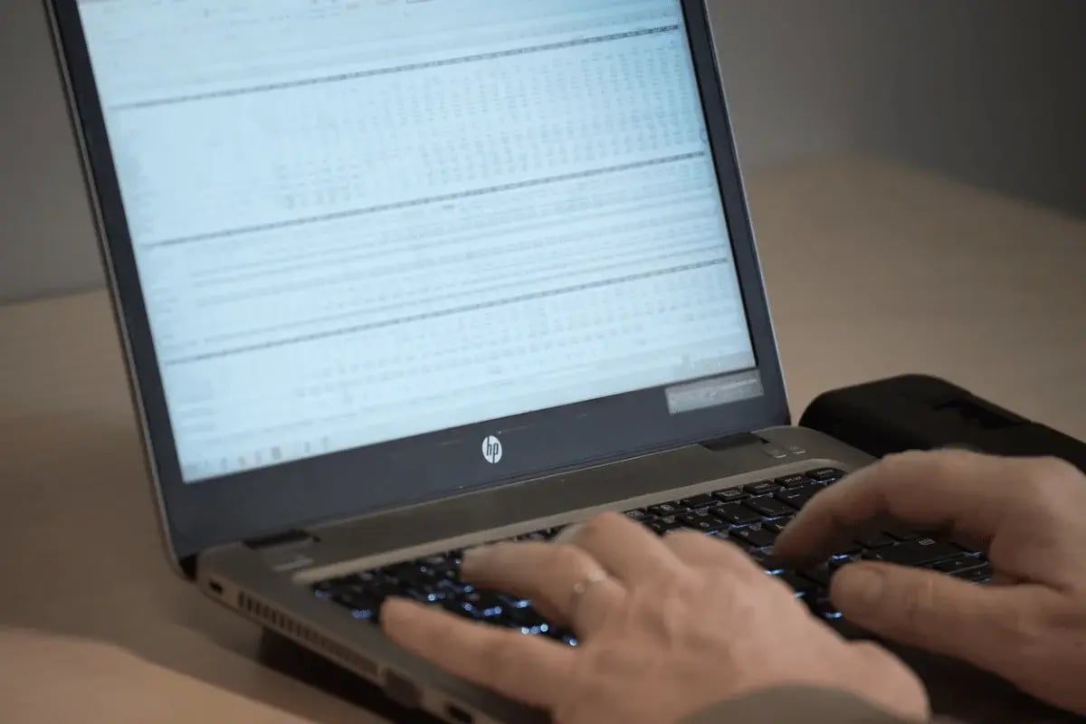 Hands typing financial data into an Excel spreadsheet on a laptop.