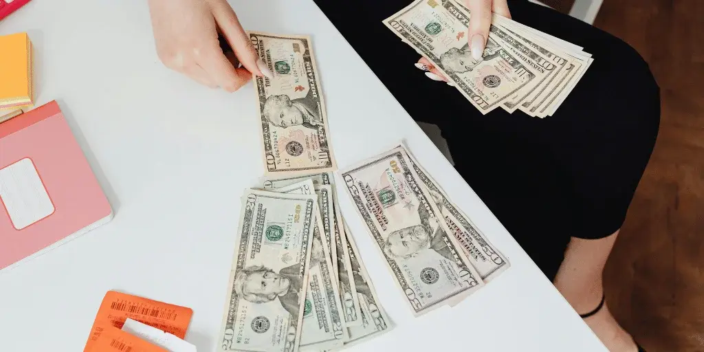 A person counting stacks of cash on a table, surrounded by colorful sticky notes and receipts.